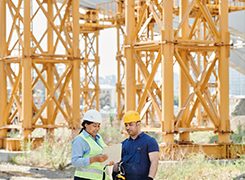 Site engineers reviewing drawings beside crane towers